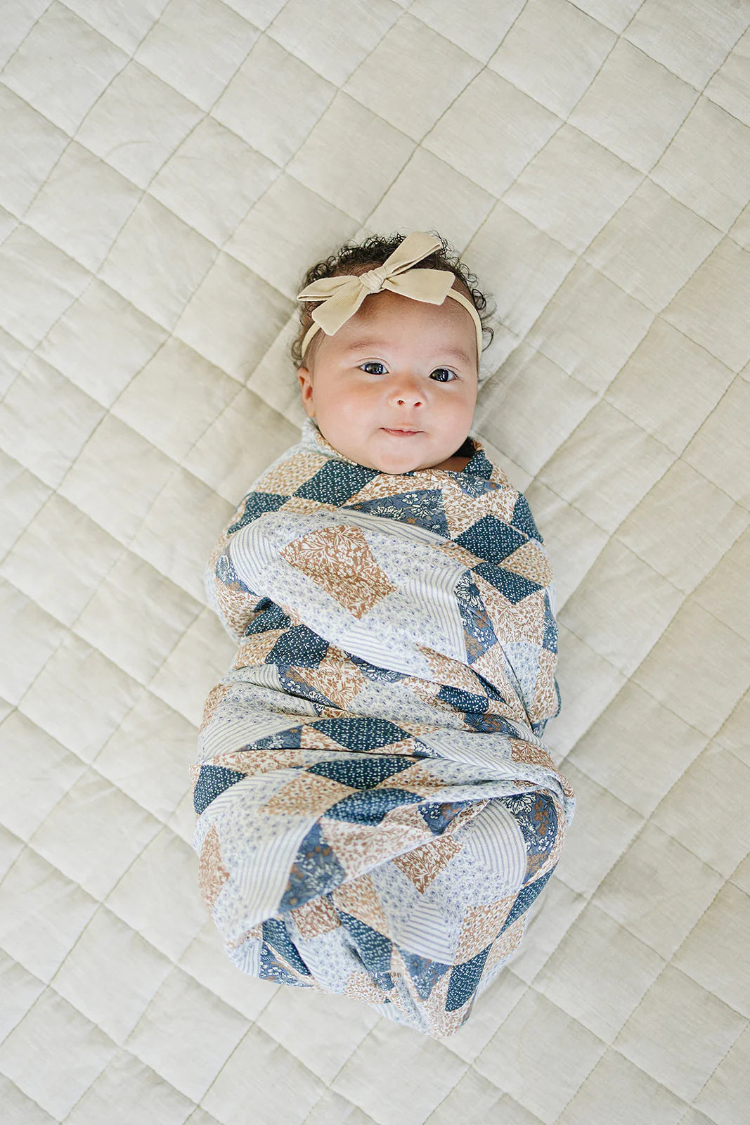 Patchwork quilt with blue, beige, and white patterns on a plain background. Mebie Baby