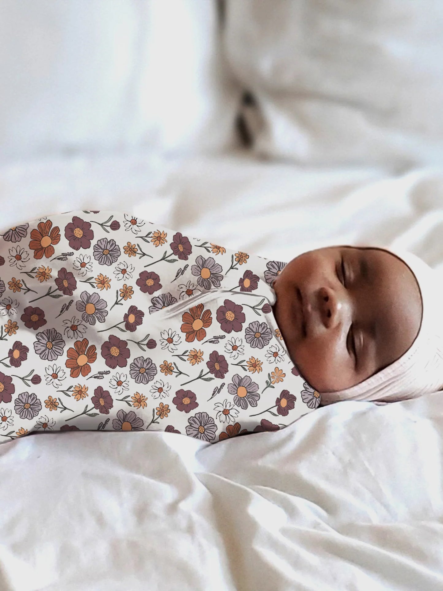 Baby swaddled in a floral patterned swaddle on a white background