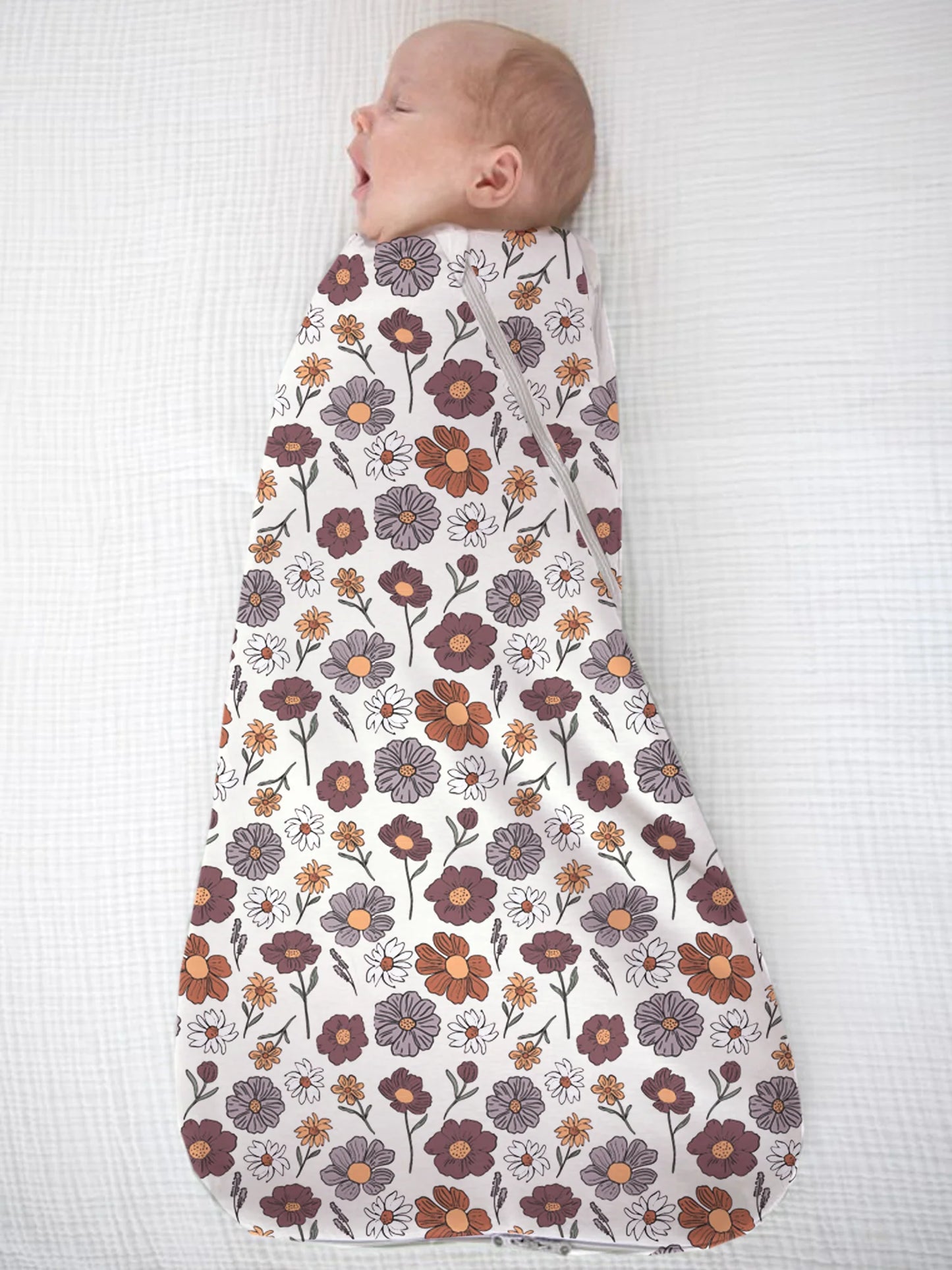 Baby swaddled in a floral patterned swaddle on a white background
