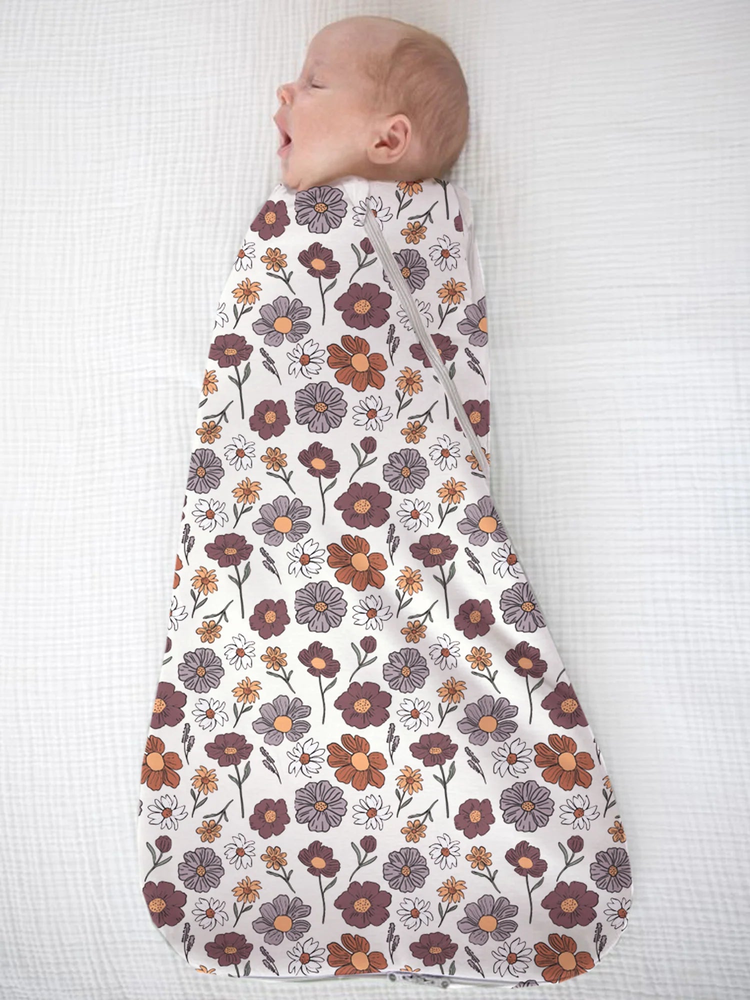 Baby swaddled in a floral patterned swaddle on a white background