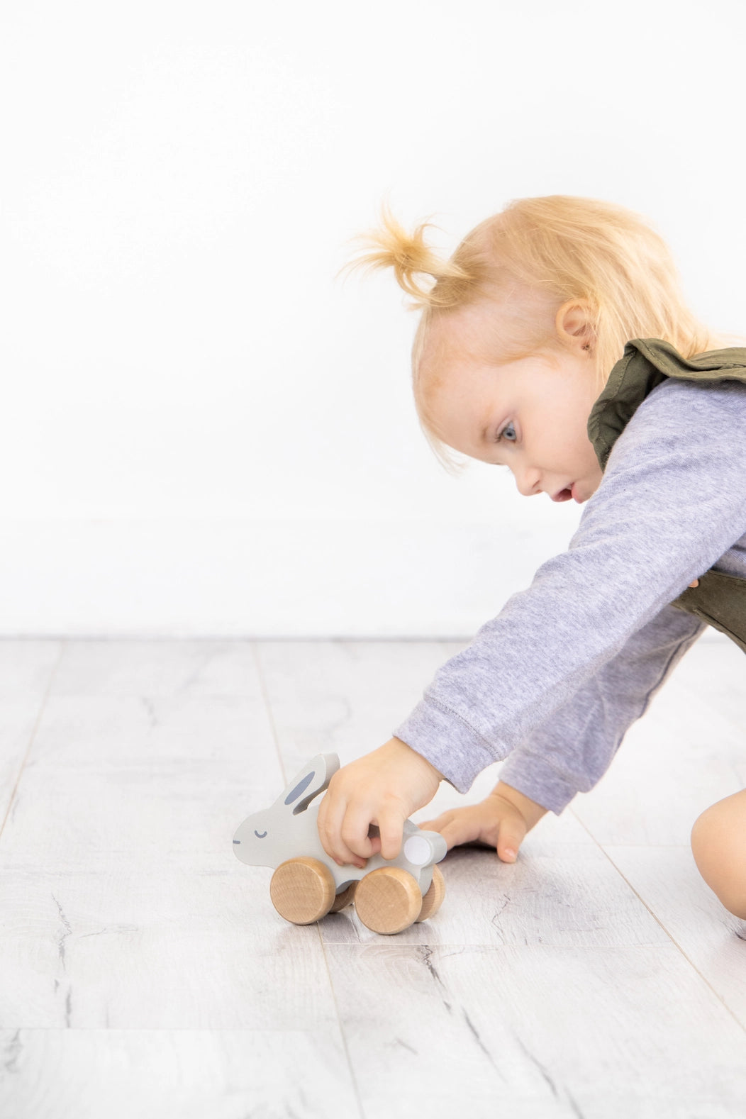 Child playing with a wooden toy on a light-colored floor.