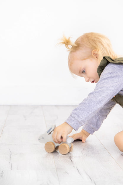 Child playing with a wooden toy on a light-colored floor.